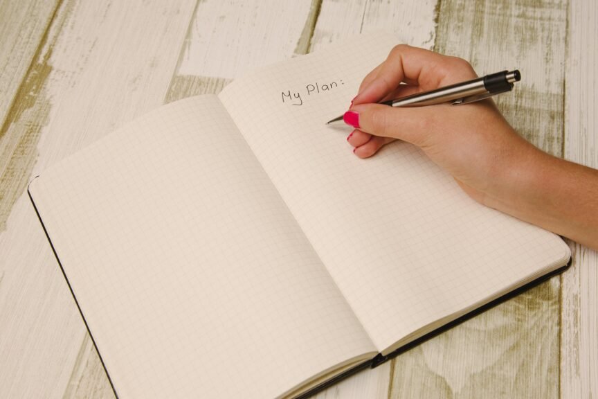 A hand is writing in a journal that starts with "my plan."
